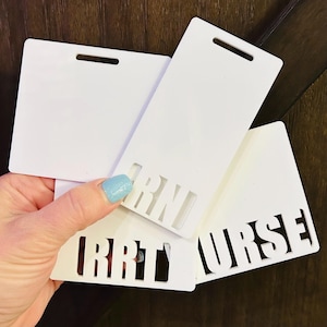 May include: Four white plastic name tags with cut-out lettering. The lettering on the tags reads "RN", "RT", and "NURSE".
