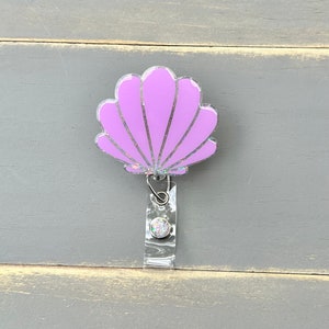 May include: A purple glitter seashell badge reel with a clear retractable badge holder.