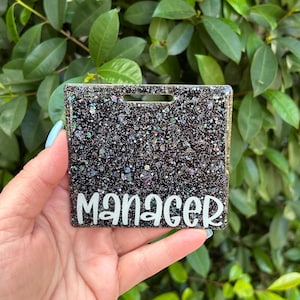 May include: Black glitter name tag with the word "Manager" in white lettering.