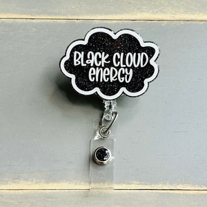 以下が含まれることがあります： 黒いグリッター仕上げの雲型バッジリールで、白い文字で「BLACK CLOUD ENERGY」とスタイリッシュなフォントで書かれています。バッジリールには、金属製のスナップボタンが付いた透明なプラスチックストラップと、身分証を保持するための伸縮式コード機構が含まれています。