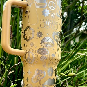 May include: A yellow stainless steel travel mug with a handle. The mug features a retro 70s design with mushrooms, peace signs, flowers, and the word "LOVE" printed on it.