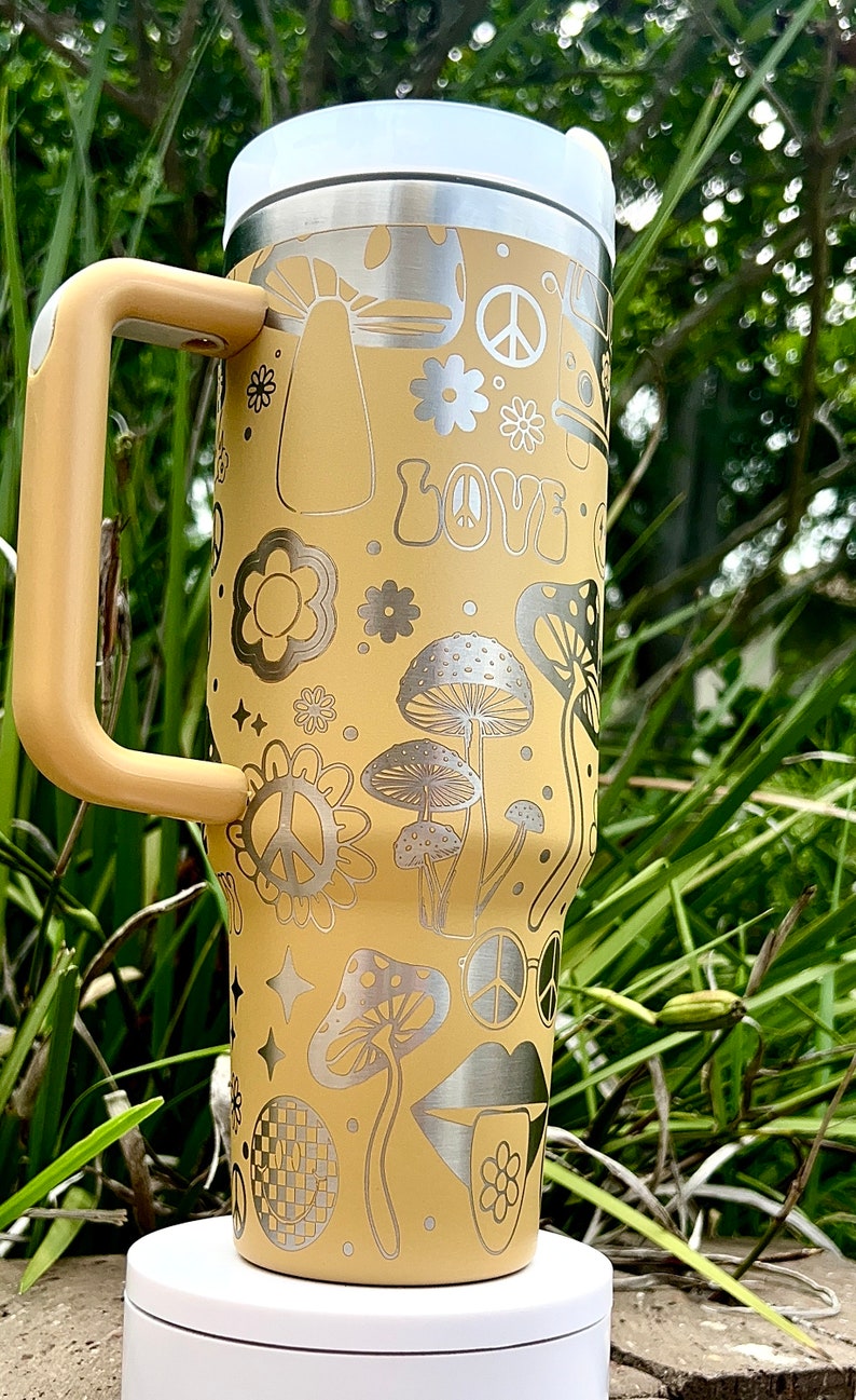May include: A yellow stainless steel travel mug with a handle. The mug features a retro 70s design with mushrooms, peace signs, flowers, and the word "LOVE" printed on it.