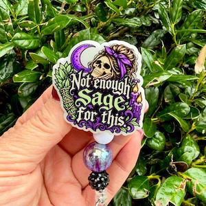 Puede incluir: Un portatarjetas con una pegatina troquelada que muestra una calavera con una diadema morada, una luna creciente, un manojo de salvia y dos velas moradas. El texto dice Not enough Sage for this. Debajo hay tres cuentas: una blanca, una morada iridiscente y una negra texturizada.