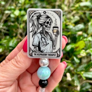 May include: A rectangular badge reel featuring a black and white illustration of a skeleton wearing a medical scrub top and stethoscope while holding a coffee cup. The text THE RESPIRATORY THERAPIST is printed at the bottom. It has a beaded lanyard.