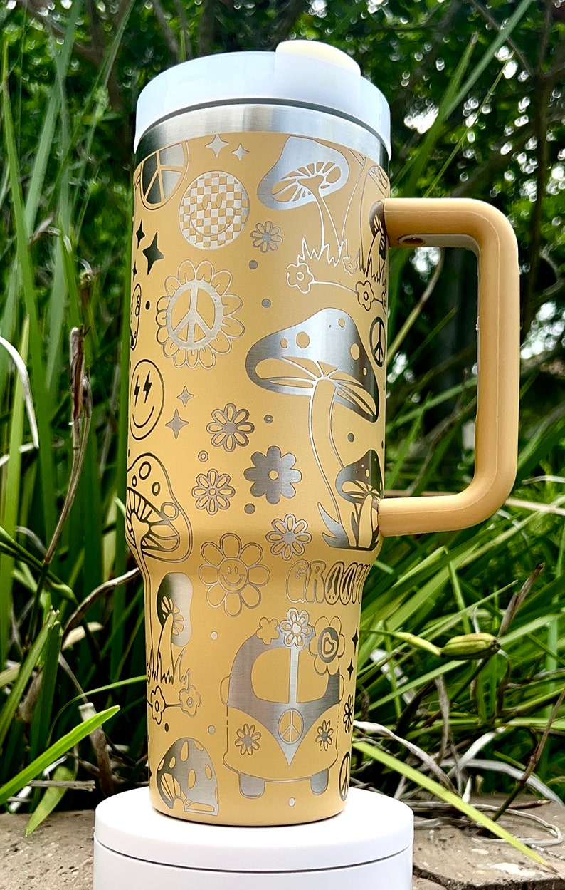 May include: A yellow stainless steel travel mug with a white lid and a brown handle. The mug is decorated with a psychedelic pattern of peace signs, mushrooms, flowers, and a van. The text "Groovy" is also visible on the mug.