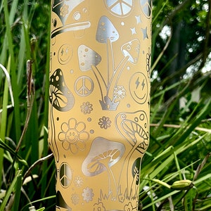 May include: A yellow stainless steel tumbler with a white lid. The tumbler features a psychedelic design with peace signs, mushrooms, flowers, and smiley faces.