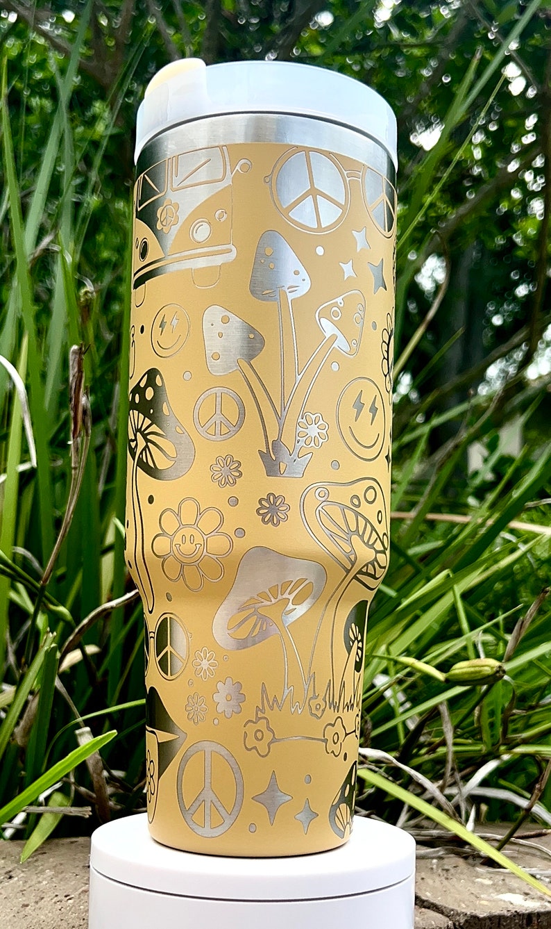 May include: A yellow stainless steel tumbler with a white lid. The tumbler features a psychedelic design with peace signs, mushrooms, flowers, and smiley faces.