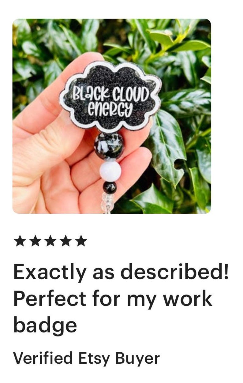 以下が含まれることがあります： 黒いグリッター仕上げの雲型バッジリール。白い文字で「BLACK CLOUD ENERGY」とスタイリッシュなフォントで書かれています。伸縮式のコードには、黒、白、透明の3つのビーズが装飾されており、先端にはプラスチック製のクリップが付いています。