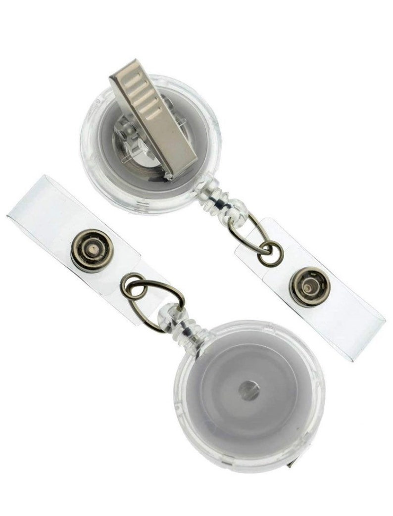 May include: Two clear retractable badge reels with a silver clip and a clear plastic strap. The reels are designed to hold a badge or ID card.