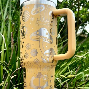 May include: A yellow stainless steel tumbler with a groovy 70s design featuring mushrooms, peace signs, flowers, and a vintage van. The tumbler has a lid and a handle.