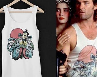 May include: A white tank top featuring a graphic print of a stylized character with a long beard, wearing ornate robes with dragon motifs, positioned in front of a large red circle. The design includes intricate blue, green, and pink details.