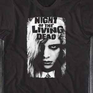 Pu&ograve; includere: Maglietta nera con una stampa grafica bianca di un viso femminile e il testo "NIGHT OF THE LIVING DEAD".