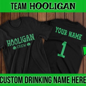 Puede incluir: Camiseta negra con texto verde que dice "Hooligan Crew" y un tr&eacute;bol en la parte delantera. La parte posterior de la camiseta tiene texto verde que dice "Your Name" y el n&uacute;mero "1" en verde.