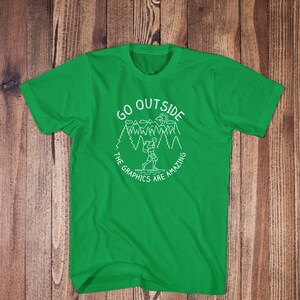 May include: Green t-shirt with a white graphic design of a person hiking in a forest with the text "Go Outside The Graphics Are Amazing".