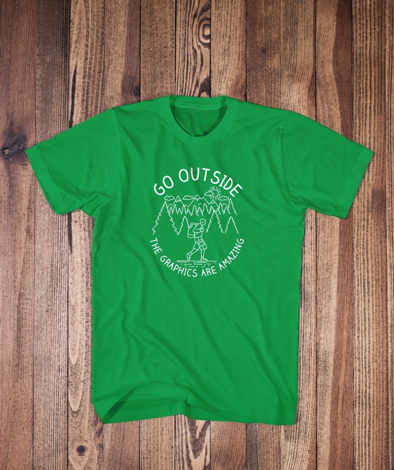 May include: Green t-shirt with a white graphic design of a person hiking in a forest with the text "Go Outside The Graphics Are Amazing".