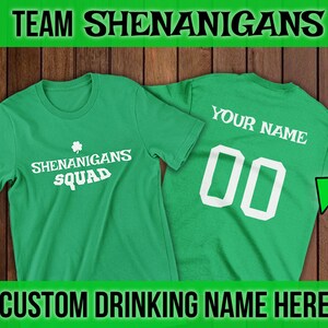 Puede incluir: Dos camisetas verdes con texto blanco. La camiseta delantera dice "Shenanigans Squad" con un tr&eacute;bol. La camiseta trasera dice "Your Name" con el n&uacute;mero "00".