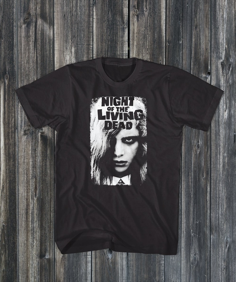 Pu&ograve; includere: Maglietta nera con una stampa grafica bianca di un viso femminile e il testo "NIGHT OF THE LIVING DEAD".