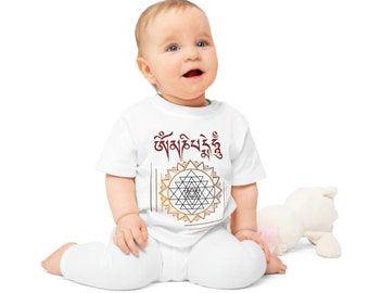 Puede incluir: Un body blanco para bebé con un diseño geométrico dorado y marrón y el texto "Om Mani Padme Hum" en rojo.