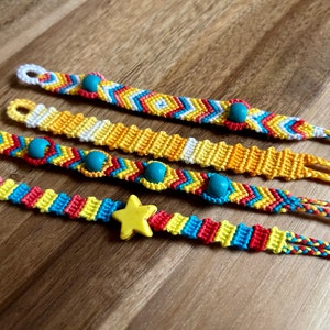 Puede incluir: Cuatro pulseras de amistad hechas a mano en colores vibrantes. Las pulseras presentan intrincados patrones tejidos con hilos azules, amarillos, rojos y blancos. Algunas tienen cuentas de madera y un dije de estrella amarilla. Un accesorio colorido.