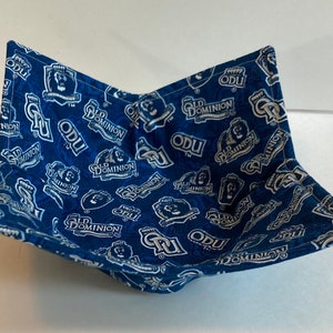 May include: A blue and white fabric bowl with the text "ODU" and "Old Dominion" repeated across the surface. The bowl is square-shaped with folded corners, creating a functional and decorative item.