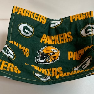 May include: Green and gold fabric bowl with a football helmet and the word "Packers" repeated on the fabric.