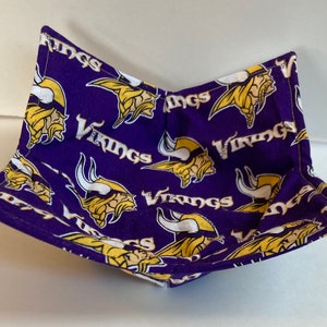 May include: Purple and gold fabric bowl cozy with a repeating pattern of the word "Vikings" and a Viking head logo. The bowl cozy is designed to be microwave-safe and is made of fabric.