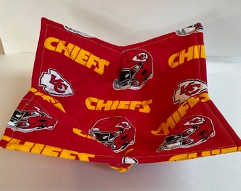 May include: A red and yellow fabric bowl featuring the Kansas City Chiefs logo and the word "CHIEFS" in yellow. The bowl has a square shape with folded corners, showcasing the team's helmet and logo.