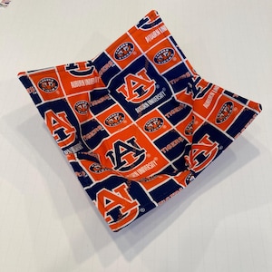 May include: A square, fabric bowl in orange and navy blue, featuring the Auburn University logo and text. The bowl is designed with a repeating pattern of the letter "A" and the words "Auburn University" and "Tigers".