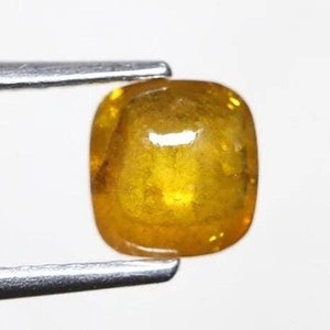 May include: A bright yellow gemstone with a cushion cut. The gemstone is held in a pair of tweezers.