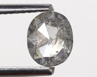 May include: A clear, oval-shaped diamond with a gray, cloudy appearance. The diamond is held in place by a pair of tweezers.