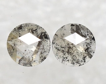 May include: Two round, faceted, gray diamonds with black inclusions. The diamonds are set in a bezel setting.