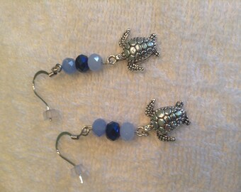 Outlander Voyager inspired, large earrings features silver plated sea turtle charms accented by tri color blue, faceted, glass beads.