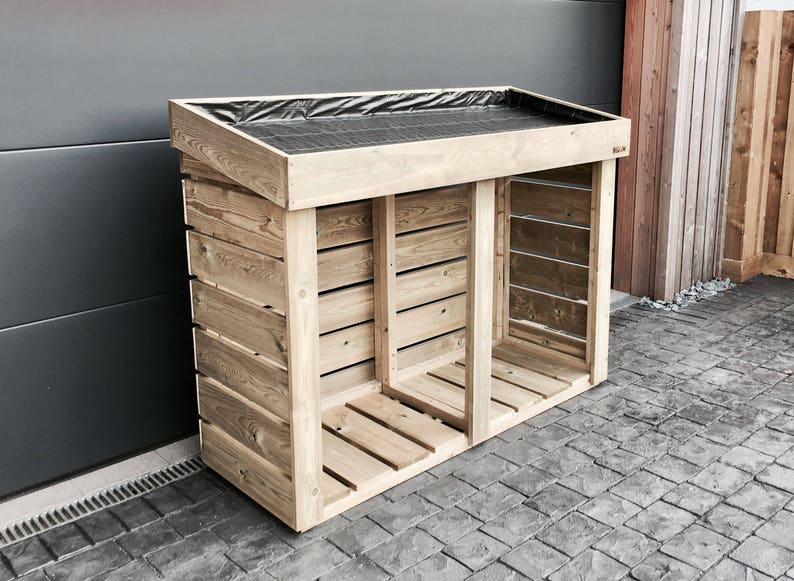 May include: A wooden log storage shed with a black weatherproof cover on the top. The shed has two compartments and is made of natural wood.