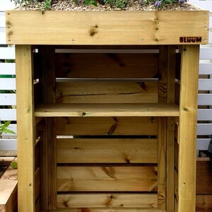 May include: A wooden shelf unit with two shelves and a planter box on top. The planter box is filled with lavender and other plants. The shelf unit is labeled "BLOOM".