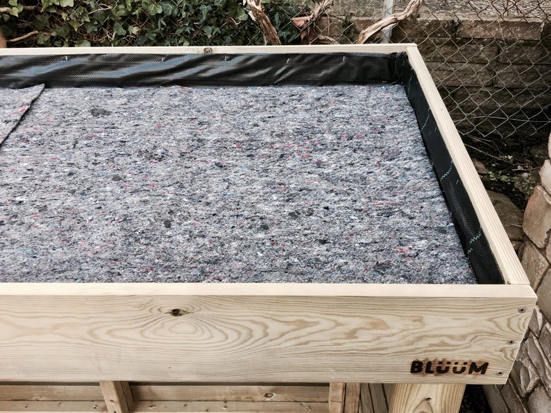 May include: A wooden raised garden bed with a black liner and a gray fabric lining. The bed is labeled "BLOOM" on the front.