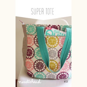 May include: A large, white tote bag with turquoise straps. The bag has a colorful pattern of circles with a vintage look. The bag has a pocket on the front with a magazine inside. The magazine has the words "NEW!" and "LOVE" on the cover. The bag is labeled "noodlehead #531".