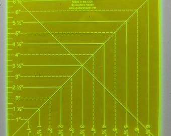 May include: A neon yellow quilting ruler with black markings and measurements in inches. The ruler is square, with diagonal and horizontal lines for precise cutting. Text on the ruler reads "Made in the USA By Quilters Haven www.quiltershaven.net".
