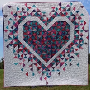 May include: A white quilt with a large pink and blue heart design made of patchwork triangles. The heart is surrounded by smaller triangles in a similar color scheme.