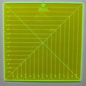 May include: A square, transparent neon green quilting ruler with measurements in inches. The ruler has a grid pattern with diagonal lines and markings from 1 to 8.5 inches. Text on the ruler reads "Made in the USA By Quilters Haven".