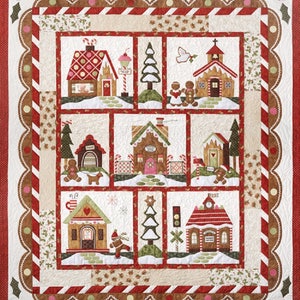 May include: A colorful patchwork quilt featuring a gingerbread village with houses, trees, and gingerbread people. The quilt is framed with a scalloped border in red, brown, and white.