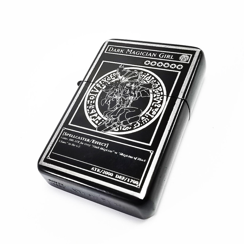 May include: Black and silver lighter with a graphic of the "Dark Magician Girl" card from the Yu-Gi-Oh! Trading Card Game. The card text reads "SPELLCASTER/EFFECT" and "ATK/2000 DEF/1700".