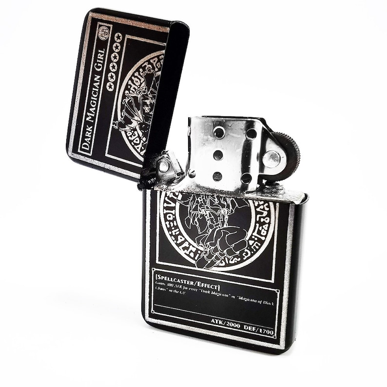 May include: A black and silver lighter with a Dark Magician Girl card design. The lighter is open and the card design is visible on both the top and bottom of the lighter. The card text reads "[SPELLCASTER/EFFECT]  Level 7 DARK Spellcaster/Effect  ATK/2000 DEF/1700".
