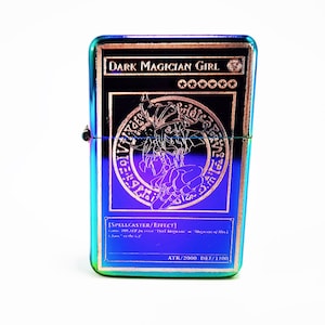 May include: A metallic lighter with a rainbow iridescent finish featuring a Dark Magician Girl Yu-Gi-Oh! card design. The card art shows the character in a purple circle with a gold border. The card text reads "DARK MAGICIAN GIRL" and "[SPELLCASTER/EFFECT]" with the attack and defense points listed as "ATK/2000 DEF/1700".