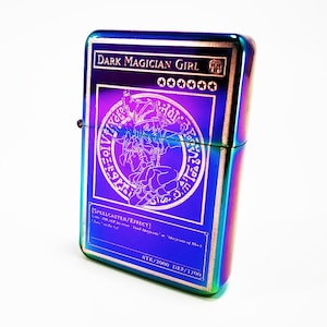 May include: A rainbow-colored metal lighter with an image of the Dark Magician Girl card from the Yu-Gi-Oh! Trading Card Game. The card text reads "[SPELLCASTER/EFFECT]" and "ATK/2000 DEF/1700".