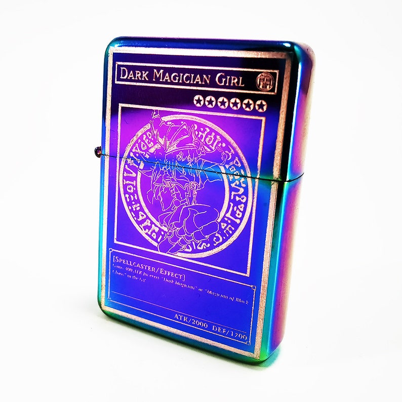 May include: A rainbow-colored metal lighter with an image of the Dark Magician Girl card from the Yu-Gi-Oh! Trading Card Game. The card text reads "[SPELLCASTER/EFFECT]" and "ATK/2000 DEF/1700".