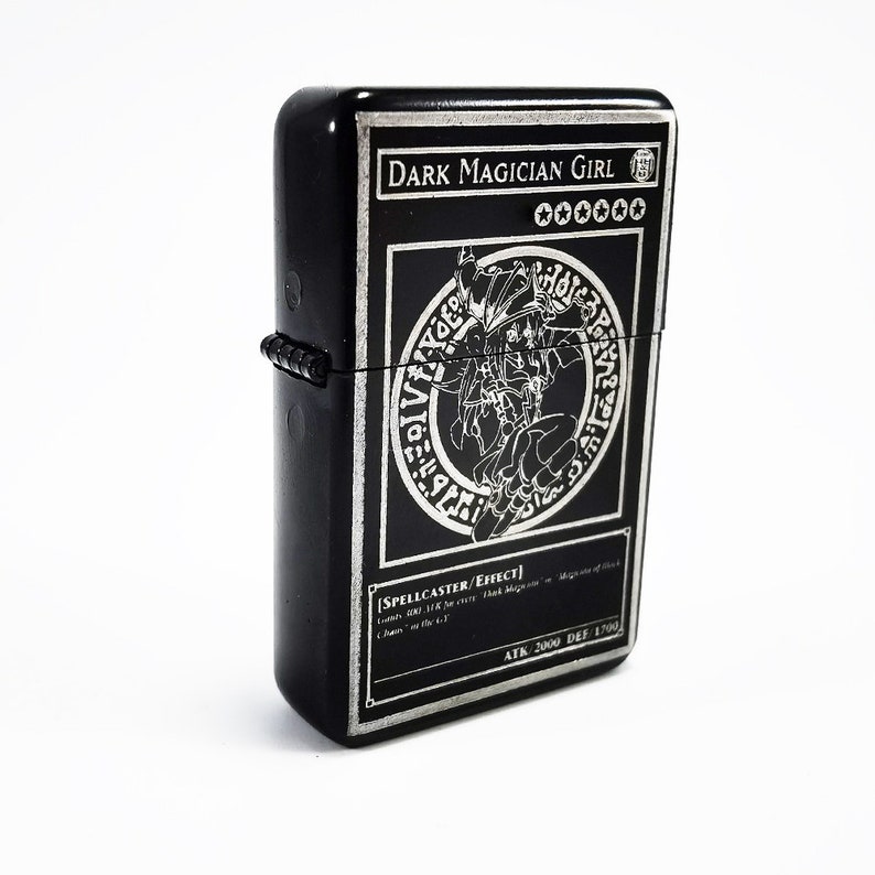 May include: Black lighter with a silver engraving of a Dark Magician Girl Yu-Gi-Oh! card. The card features a black and white illustration of the character with the text "DARK MAGICIAN GIRL" and "SPELLCASTER/EFFECT".