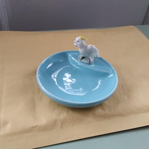May include: A light blue ceramic dish with a divided section and a white cockatoo figurine with a yellow crest.