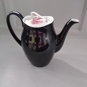 May include: Black ceramic coffee pot with a white lid featuring a pink rose design.