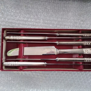 Peut inclure: Un ensemble de cinq couteaux à steak en argent plaqué dans une boîte rouge. Les couteaux ont des manches ornés et sont disposés en rangée.