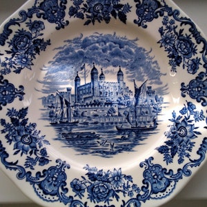 Peut inclure: Une assiette en céramique blanche avec un motif bleu et blanc représentant la Tour de Londres. L'assiette a un bord festonné et une bordure florale.